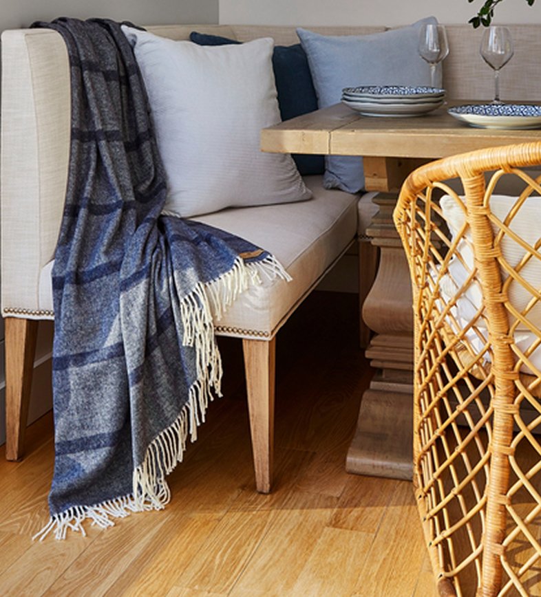 Blue and grey plaid wool throw blanket with cream fringe draped over an upholstered dining bench